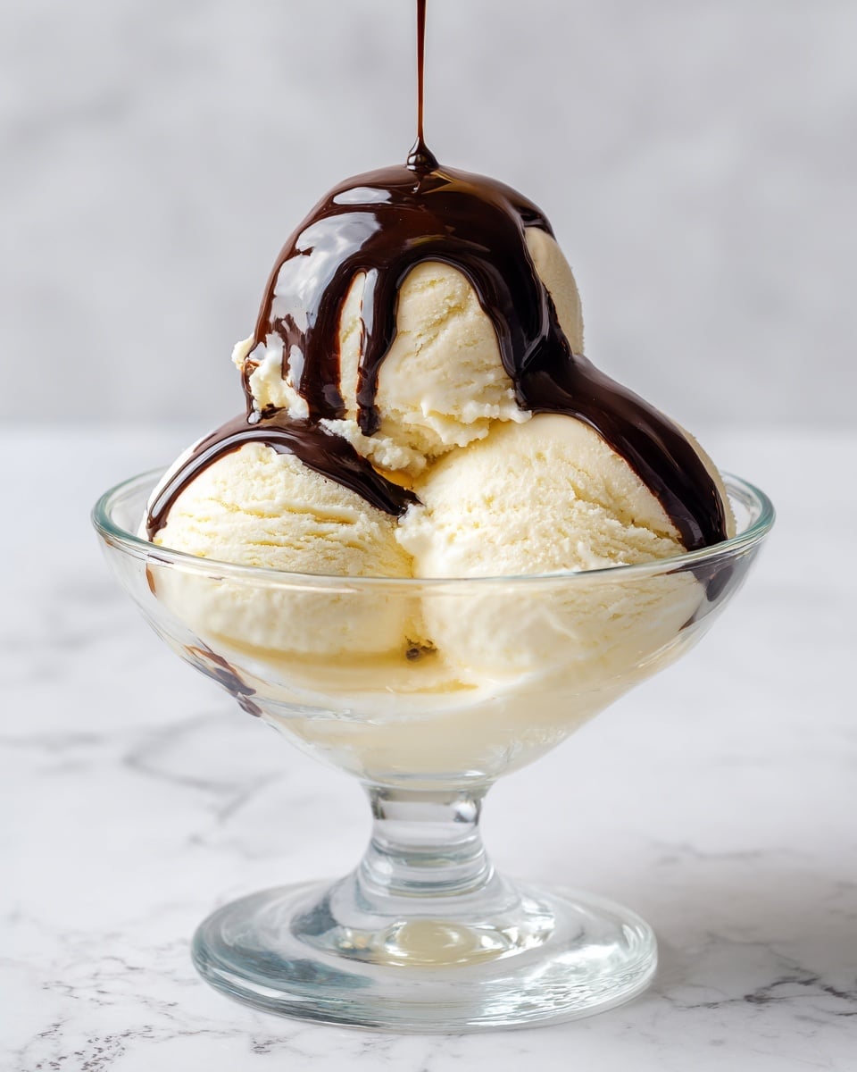 A clear glass dessert bowl holds two large scoops of pale yellow vanilla ice cream. The top of the ice cream is covered with thick, dark brown chocolate syrup that drips slightly on the sides. Brightly colored rainbow sprinkles are scattered on the chocolate syrup, adding small pops of red, orange, yellow, green, blue, and purple. A shiny metal spoon is placed into the ice cream from the left side of the bowl. In the background, there is a small white bowl filled with more colorful sprinkles and a glass jar of chocolate syrup, all set on a white marbled surface. photo taken with an iphone --ar 4:5 --v 7