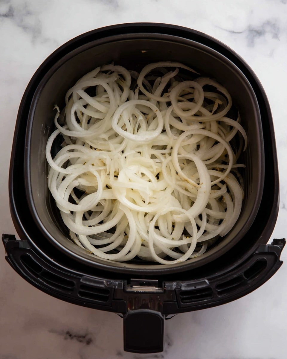 Inside a black air fryer basket with a metal mesh bottom, there is a single layer of thin, crispy fried onions. The onions are golden brown with some lighter and darker shades, showing a crunchy texture. The air fryer is sitting on a white marbled surface, and the basket has a gray handle at the front. The background includes the upper part of the air fryer with control markings and the brand name visible. photo taken with an iphone --ar 4:5 --v 7
