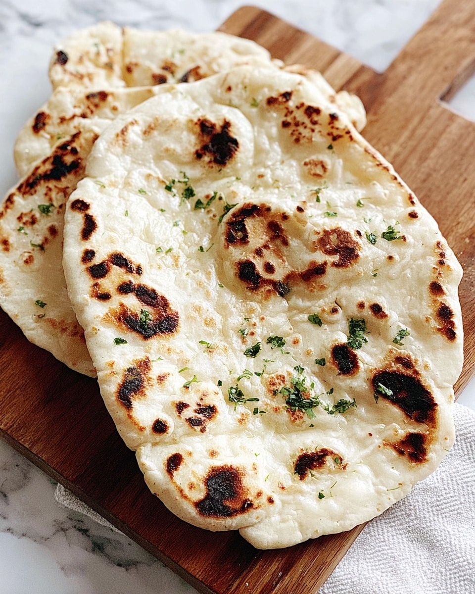 A stack of four round flatbreads with a slightly uneven shape is placed directly on a soft beige cloth. Each flatbread has a pale golden color with dark brown char marks scattered unevenly across the surface. Small bits of green herbs and white sesame seeds are sprinkled on the top flatbread, adding a fresh and textured look. The flatbreads have a soft, slightly puffed texture with some air pockets visible. The background is softly blurred fabric. Photo taken with an iphone --ar 4:5 --v 7