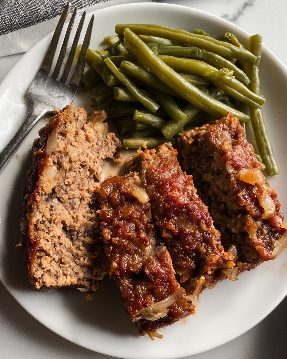 A white plate on a white marbled surface holds two main sections of food: one side with a pile of cooked green beans, soft and slightly glossy with a mix of light and dark green shades, arranged loosely. The other side has three thick slices of meatloaf, showing a rough texture colored brown with visible bits of onion and some orange bits, with a slightly crispy darker brown crust on the edges. A shiny metal fork rests on the left edge of the plate. Photo taken with an iphone --ar 4:5 --v 7