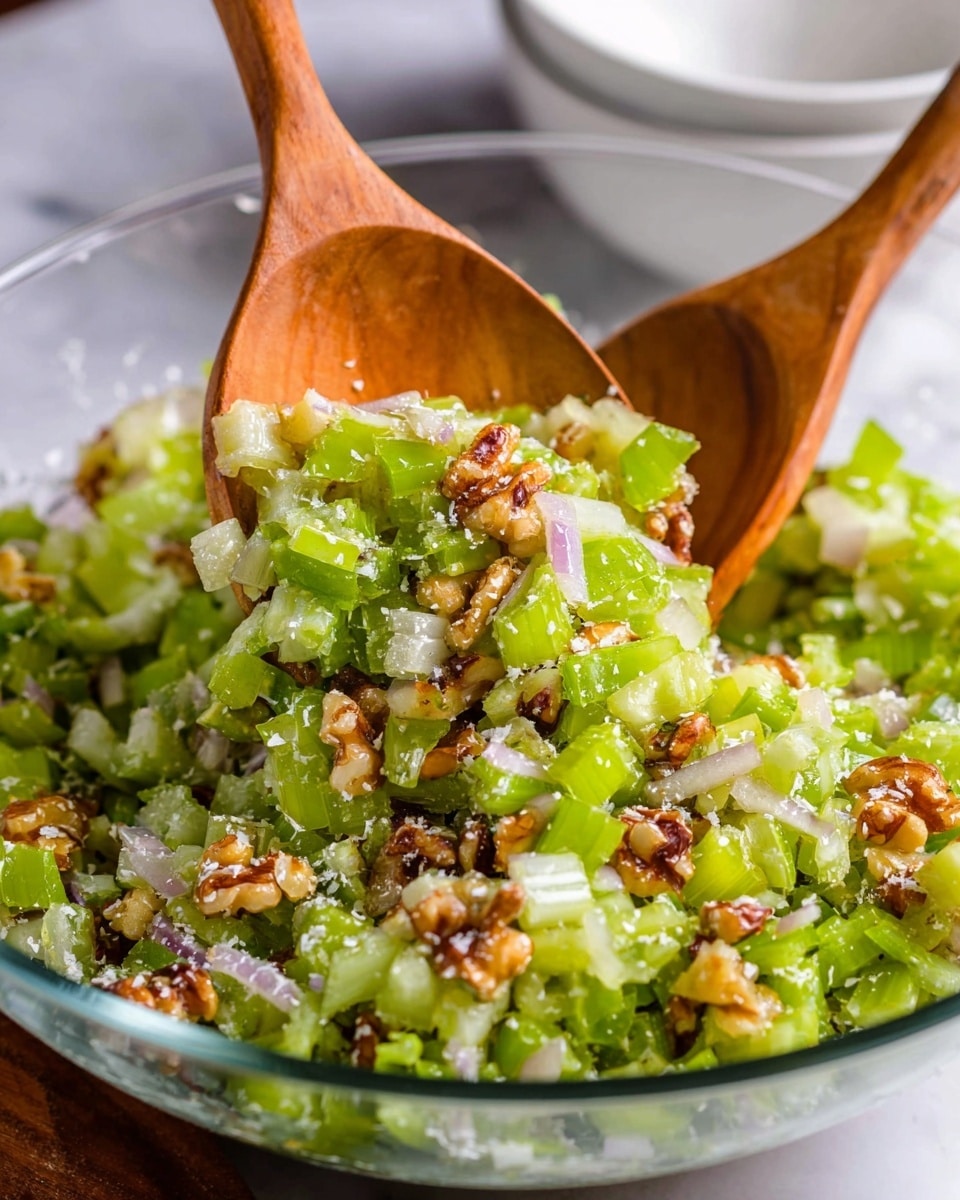 A clear bowl filled with a mix of chopped green celery pieces, thin slices of light purple shallots, small bits of brown nuts, and golden raisins, all lightly sprinkled with a powdery white ingredient. Two wooden spoons lift some of the salad, showing the layers of fresh celery, crunchy nuts, and tender shallots mixed evenly. The background shows a white marbled surface and a blurred white bowl. photo taken with an iphone --ar 4:5 --v 7