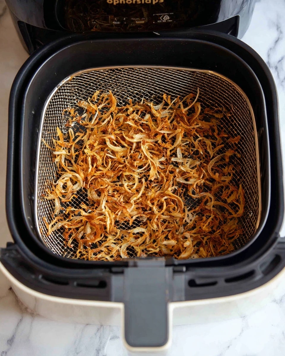 A close-up view inside a black air fryer basket filled with many thin, white onion rings stacked loosely together, showing their translucent and slightly shiny texture. The air fryer device is open, and the basket has a matte black finish with a handle at the bottom center. The scene is set on a white marbled surface. photo taken with an iphone --ar 4:5 --v 7