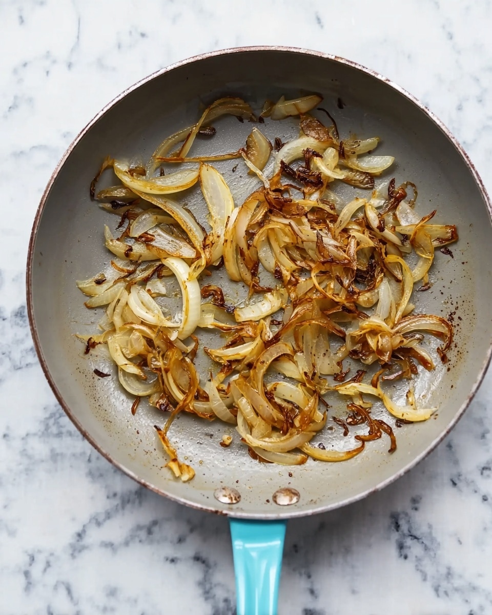 The image shows a gray frying pan with a light blue handle lying flat on a white marbled surface. Inside the pan, there are thin slices of lightly browned and caramelized onions spread unevenly across the center. The onions have different shades of golden brown with some pieces darker, showing a mix of soft and crispy textures. The pan surface has some oily spots and light residue from cooking, emphasizing the cooking process photo taken with an iphone --ar 4:5 --v 7