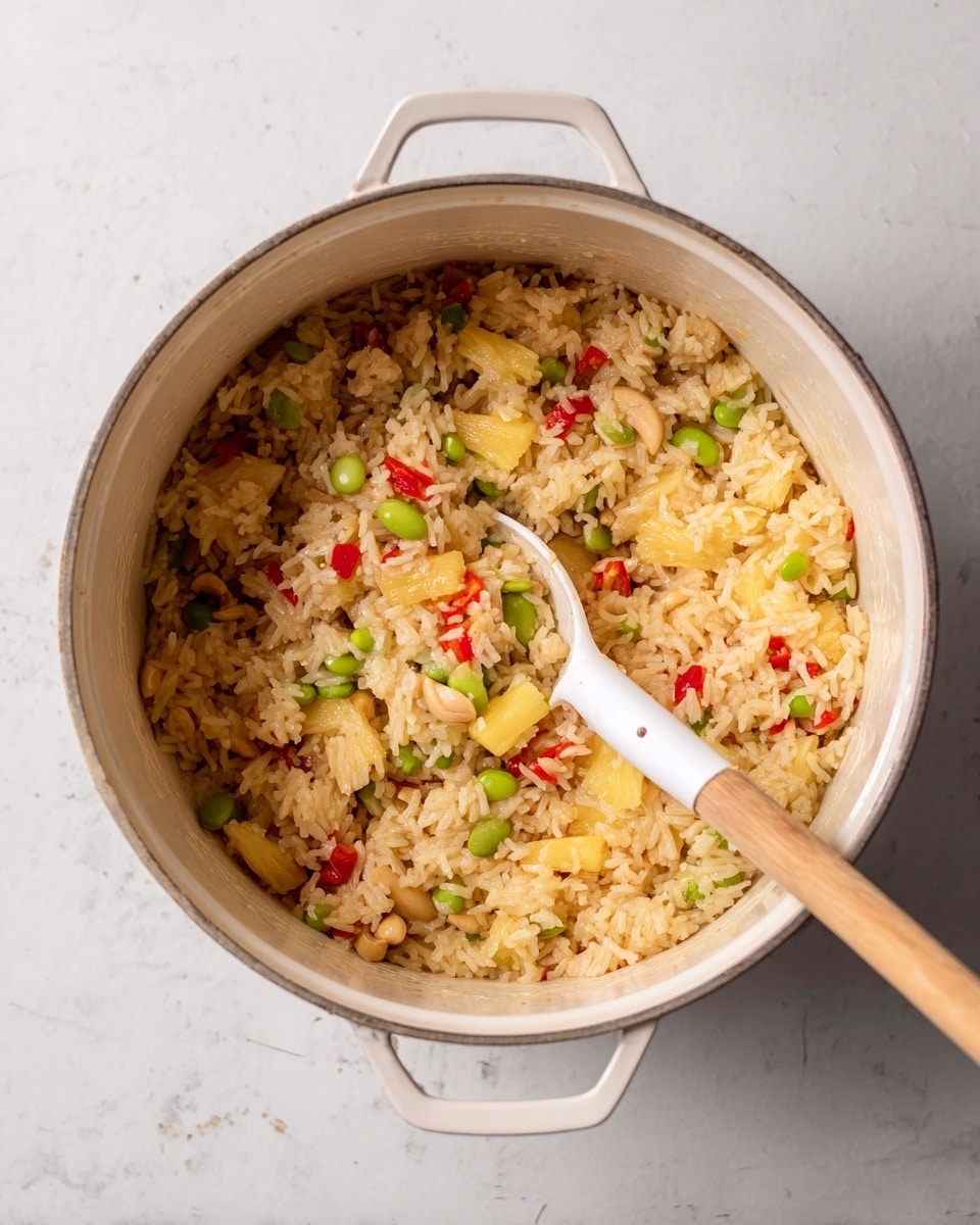 Inside a white pot filled with cooked rice, there are visible pieces of yellow pineapple, light brown cashews, green edamame beans, and small diced red bell peppers. A white slotted spoon with a wooden handle is scooping some rice mixture from inside, showing the combination of all ingredients mixed well. The pot is placed on a white marbled surface that adds a clean and light background to the scene. photo taken with an iphone --ar 4:5 --v 7