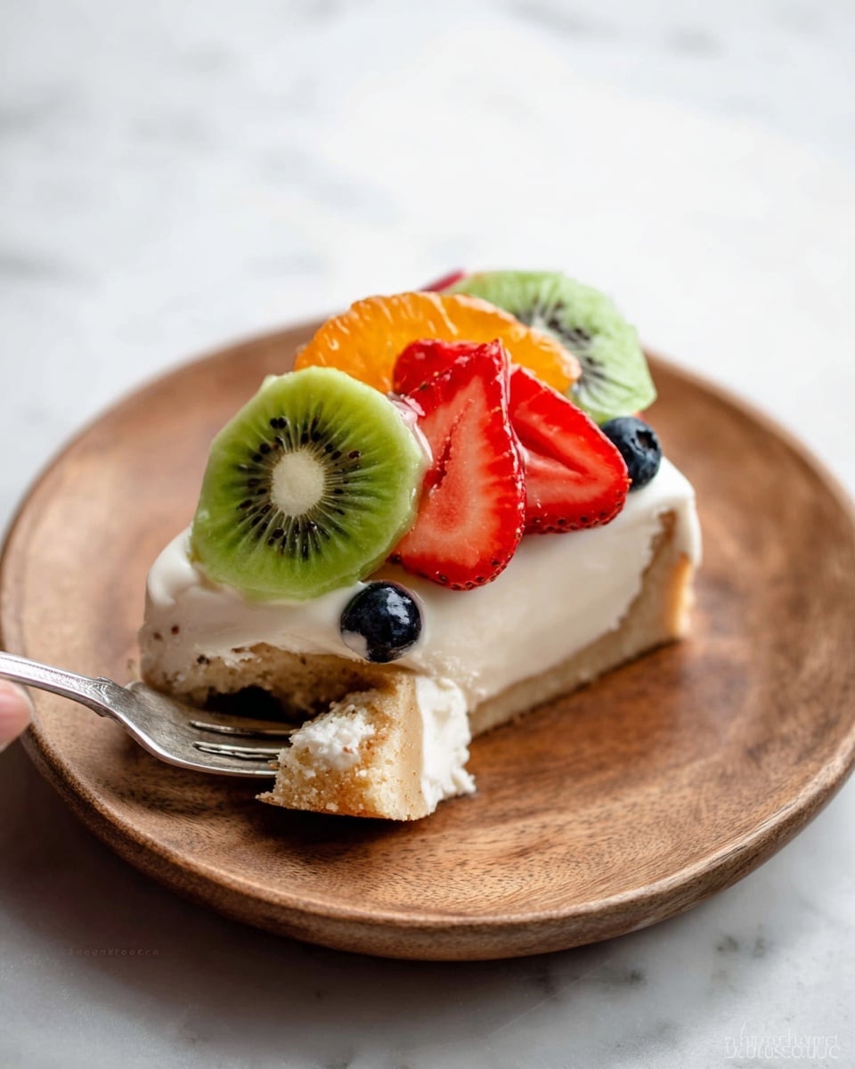 A slice of light beige cake forms the base layer on a round white wooden plate, topped with a thick layer of smooth white cream. On the cream, there are three slices of red strawberry, two halves of bright green kiwi with black seeds in the center, and two small dark blue blueberries placed near the fruits. A small piece of the cake slice is on a silver fork with some cream and a bit of an orange slice, held by a woman's hand. The scene is set on a white marbled surface. photo taken with an iphone --ar 4:5 --v 7