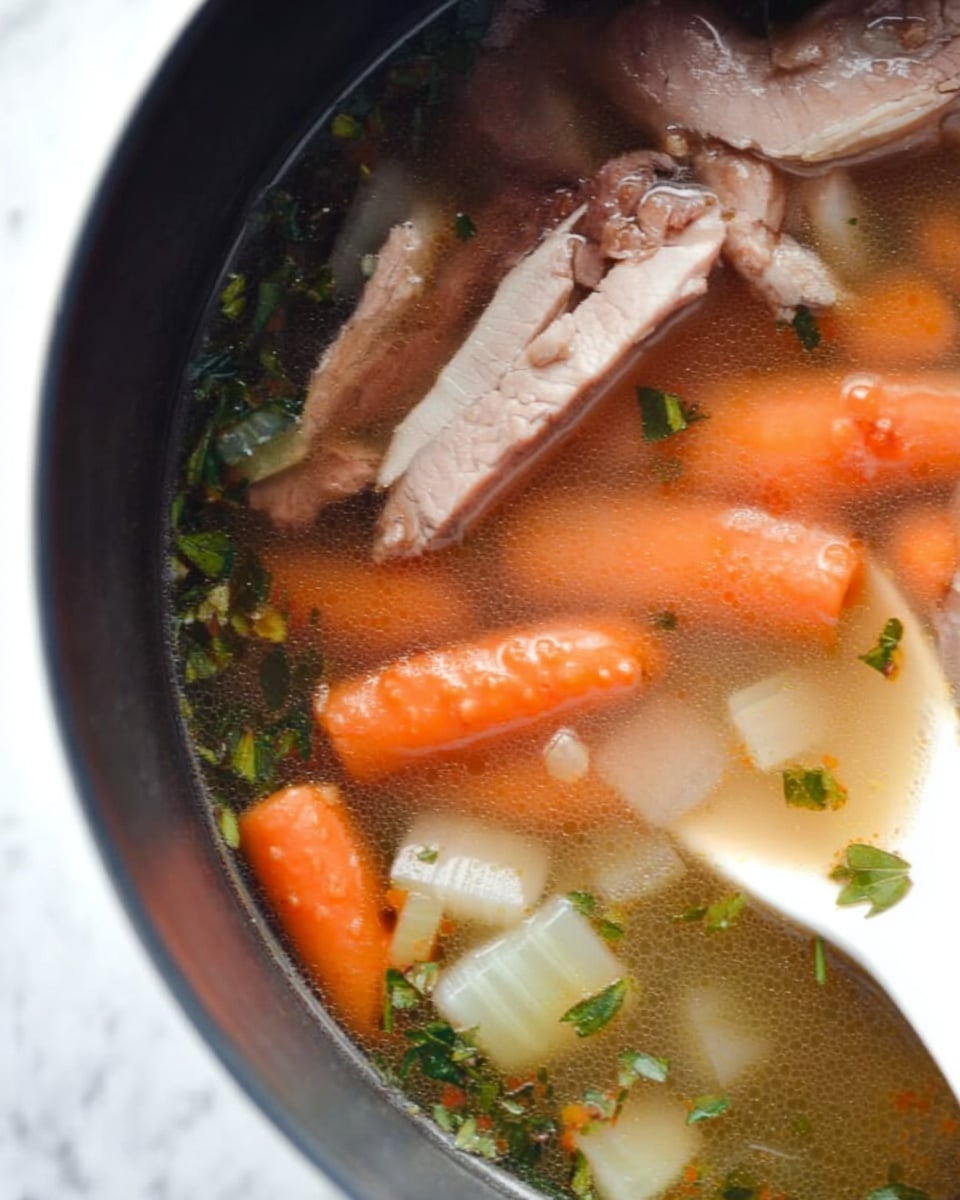 A close-up view of a pot filled with clear broth soup showing several layers of ingredients. On the top layer, thin slices of light brown meat rest on the surface. Below, there are bright orange baby carrots clustered together on the left side. On the right side and slightly below the carrots, pieces of pale white celery are partially submerged. Small green herb flakes float evenly throughout the clear liquid. The pot’s dark edge surrounds the soup, and a white spoon with some herbs is dipped in on the left side. The background shows a white marbled surface photo taken with an iphone --ar 4:5 --v 7