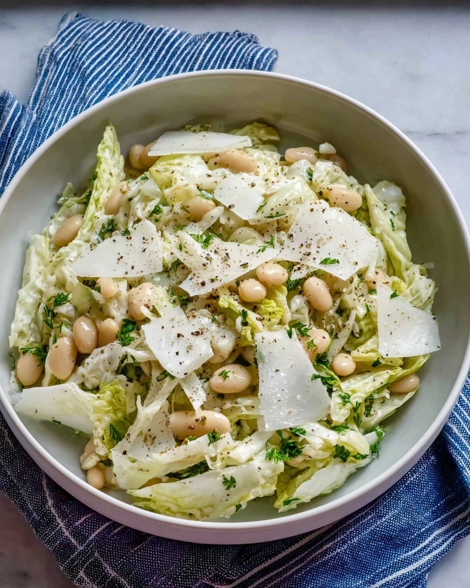 A white bowl holds a salad made of three visible layers: the bottom layer is pale sliced cabbage with a crunchy texture, the middle layer is scattered light beige beans, and the top layer has thin green herb pieces and large thin white cheese slices evenly spread across. The salad is sprinkled with black pepper, adding tiny dark specks throughout. The bowl sits on a white marbled textured surface with a blue and white striped cloth partially visible underneath. Photo taken with an iphone --ar 4:5 --v 7