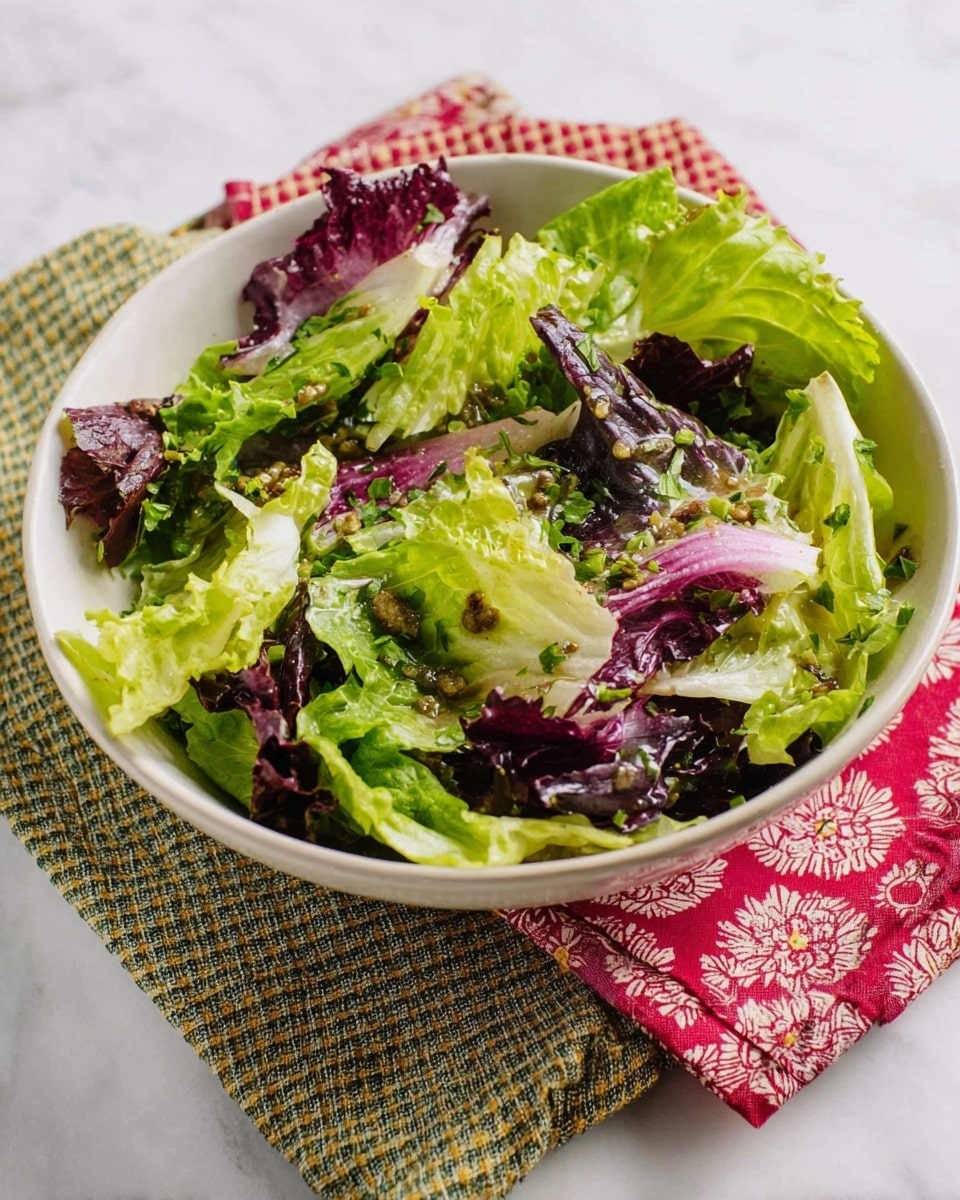 A white bowl holds a fresh salad with two main layers: the base layer has light green lettuce leaves with ruffled edges, and the top layer adds darker purple-red radicchio leaves interspersed throughout. The salad is lightly coated with a dressing that has visible small bits of green herbs and finely chopped onions, giving a slight shine to the leaves. The bowl sits on two textured cloth napkins, one with a red floral pattern and the other with a green and white check pattern, all placed on a white marbled surface. Photo taken with an iphone --ar 4:5 --v 7