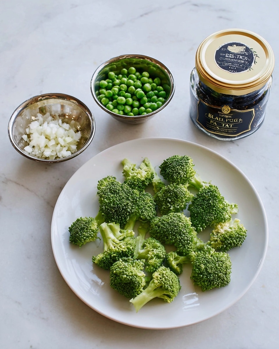 A white plate holds several bright green broccoli florets spread out evenly, showing their textured tops and stalks. To the left, there are two small silver bowls placed on a white marbled surface; one bowl contains frozen green peas with a slight frost on them, and the other bowl has finely chopped white garlic with a rough texture. Behind the bowls sits a glass jar with a gold lid and a black label, which reads