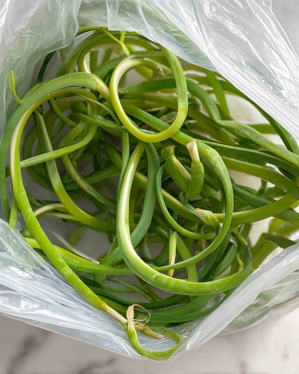 A close-up view of long, curled green garlic scapes inside a translucent plastic bag. The garlic scapes have a smooth texture with a slight shine, showing light and dark green shades. They are coiled and gently twisted, filling the bag with some loose loops and a few straighter pieces, all resting on a white marbled surface. The image is bright and clear, showing the natural color and shape of the garlic scapes. photo taken with an iphone --ar 4:5 --v 7