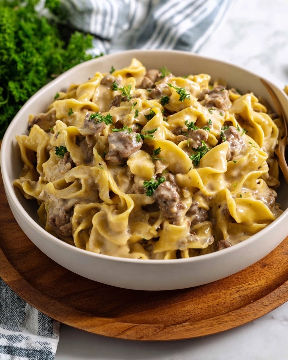 A white bowl filled with creamy pasta mixed with small pieces of cooked meat, layered evenly throughout. The pasta is light yellow with a smooth, slightly thick sauce coating each piece, giving a shiny texture. Fresh green parsley leaves are scattered on top, adding a fresh color contrast. The bowl is placed on a round wooden plate on a white marbled surface, with a soft white and blue striped cloth nearby, creating a cozy atmosphere. Photo taken with an iphone --ar 4:5 --v 7