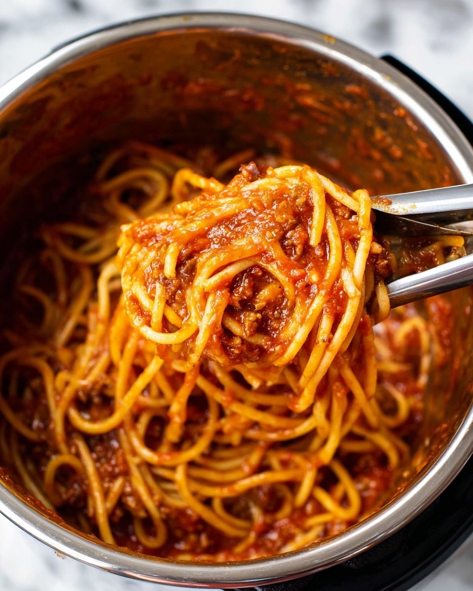 A close-up view inside a shiny metal pot shows thick spaghetti noodles mixed with rich, chunky red tomato sauce covered with small bits of meat. The sauce is thick and coats the noodles well, giving a glossy orange-red color to the pasta. A pair of metal tongs holds a small bundle of the noodles lifted above the pot. The pot sits on a white marbled surface with a blurred background. photo taken with an iphone --ar 4:5 --v 7