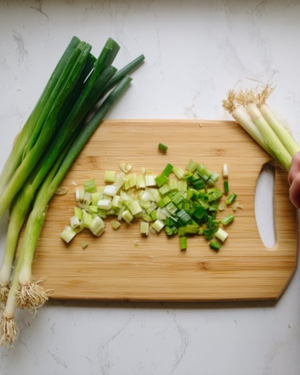 The image shows a light wooden cutting board placed on a white marbled surface. On the cutting board, there are chopped green onion pieces scattered, with some larger segments near the left edge. To the left and right of the cutting board, there are whole green onions lying on the surface, some with roots and white parts visible. A woman's hand is not shown interacting with the items. The overall color scheme is pale green and white with natural textures from the onions and the wooden board. photo taken with an iphone --ar 4:5 --v 7