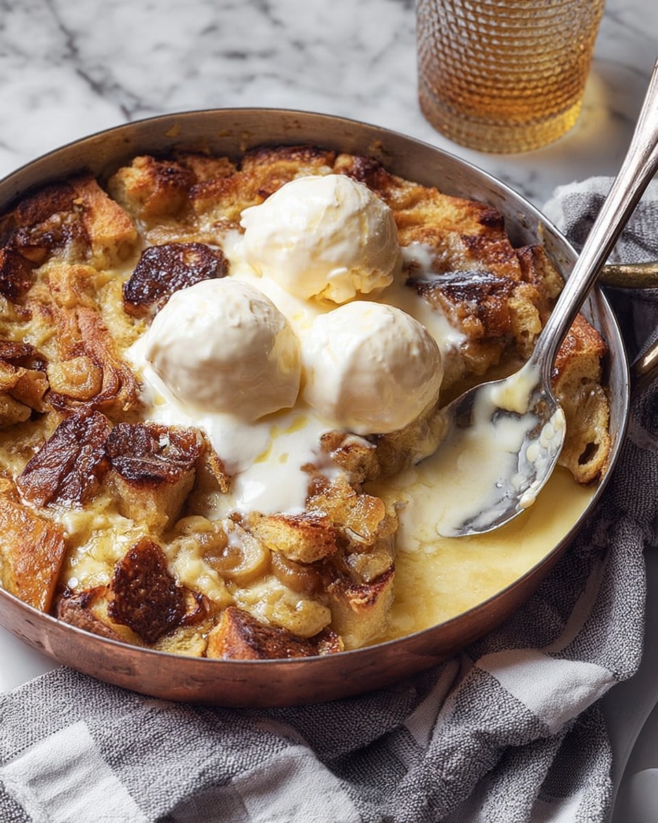 A round copper pan filled with a warm bread pudding that has a golden brown crust with some darker toasted spots, and soft, creamy bread pieces inside. On top of the pudding, there are three scoops of white creamy ice cream slightly melting, creating a glossy texture mixing with the pudding’s surface. A large metal spoon rests on the right side, partly inside the pudding. The pan sits on a white marbled surface with a folded grey and white checkered cloth under one side, and a glass drink with a textured pattern is blurred in the background. Photo taken with an iphone --ar 4:5 --v 7