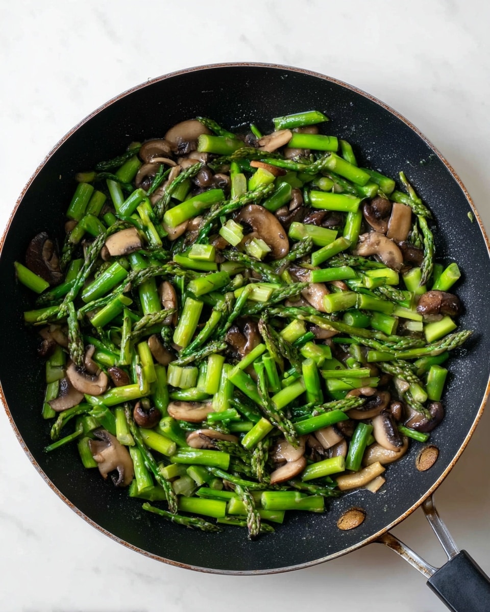 A black skillet filled with bright green asparagus stalks cut into small pieces mixed with sliced brown mushrooms, all cooked and spread evenly in the pan. The skillet handle is visible on the right side, resting on a white marbled surface. The colors are simple, mostly green and brown, with a touch of light reflecting on the vegetable surfaces. photo taken with an iphone --ar 4:5 --v 7