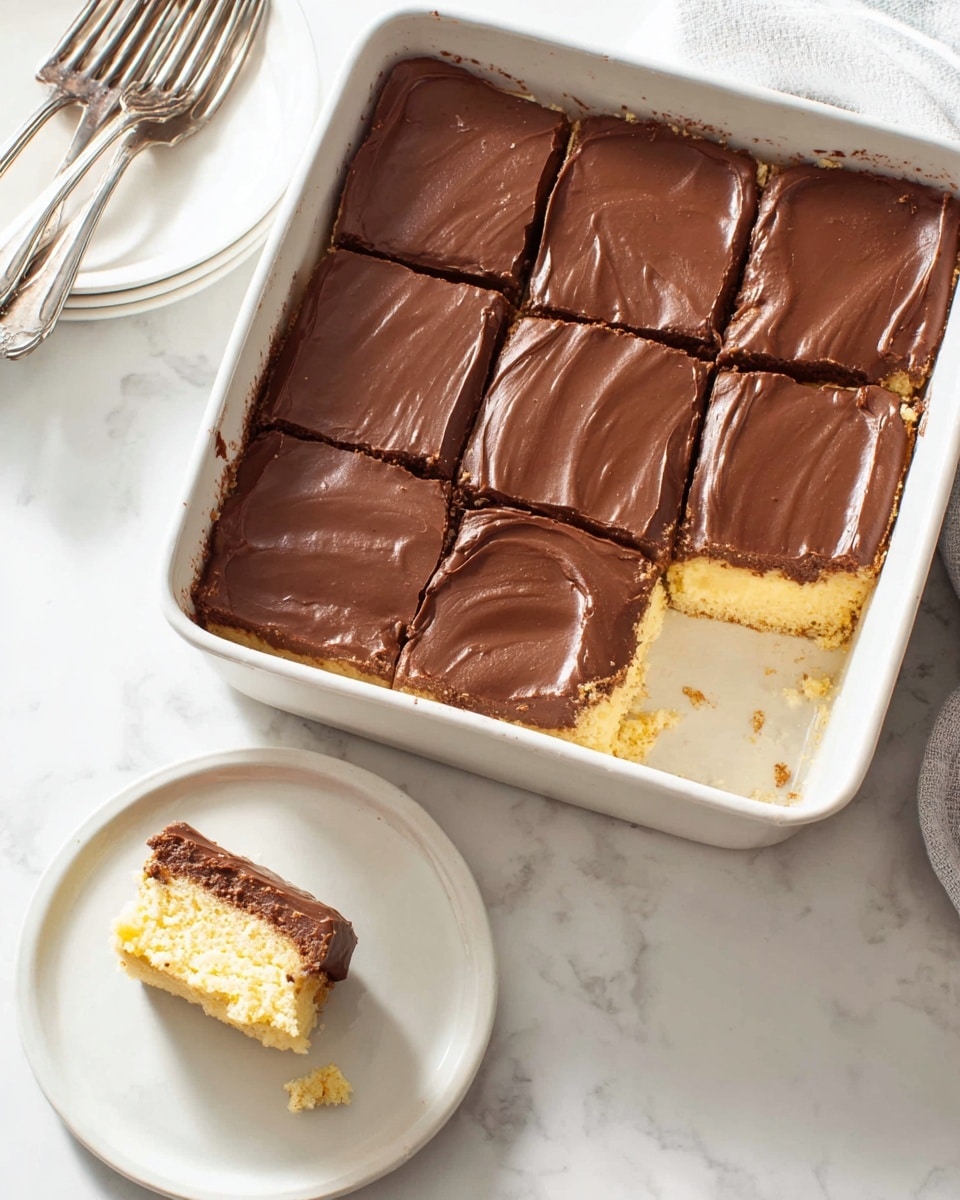 A white rectangular dish holds a square chocolate-topped dessert cut into nine pieces. The top layer is smooth, dark brown chocolate spread evenly over a thick, light yellow cake layer beneath it. One piece is missing from the dish, showing the soft, spongy cake. Nearby, a small white plate has one piece of the dessert with visible layers and slight crumbs around it. The setting includes a white marbled surface and a white dish with two silver forks in the background. photo taken with an iphone --ar 4:5 --v 7