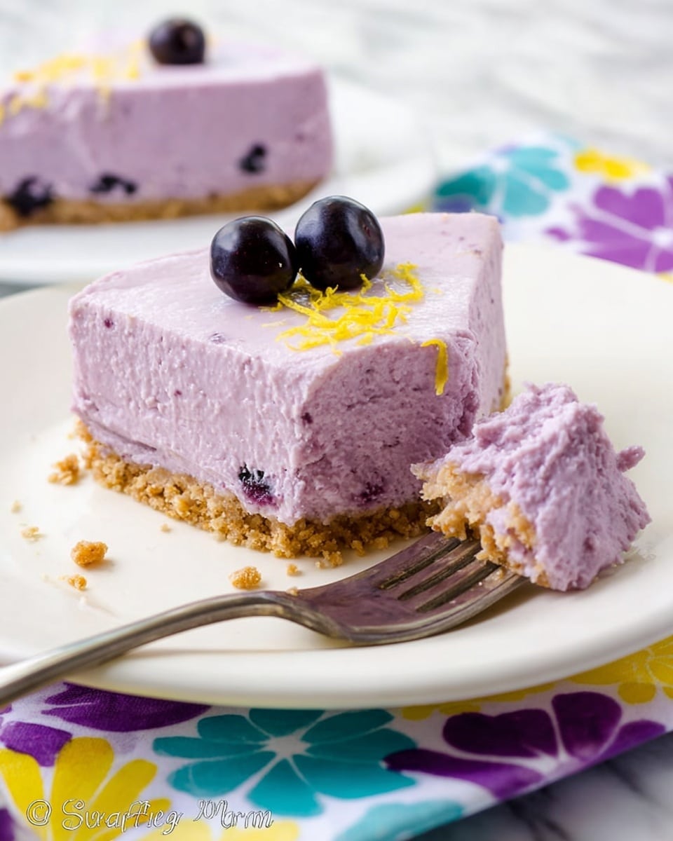 A square slice of light purple cheesecake sits on a white plate with a crumbly, light brown base layer. The top layer of the cheesecake is smooth and creamy with a few darker purple specks inside, and it is decorated with three dark blueberries and small bits of yellow zest. Beside the slice, a fork holds a bite-sized piece showing the thick purple cheesecake on a crumbly crust. The plate rests on a colorful fabric with purple, blue, yellow, and white flower shapes. The surface beneath is a white marbled texture. Photo taken with an iphone --ar 4:5 --v 7
