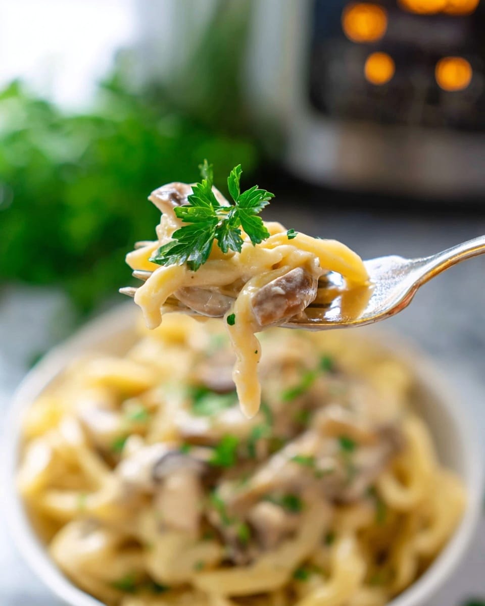 A close-up view of a fork holding a bite of creamy pasta with three layers: the pasta is pale yellow with a smooth, thick sauce coating it, small pieces of light brown mushrooms, and a bright green parsley leaf on top. The background shows more pasta in a white bowl sitting on a white marbled surface, slightly blurred, with a touch of green herbs and a soft, natural light softly illuminating the scene. Photo taken with an iphone --ar 4:5 --v 7