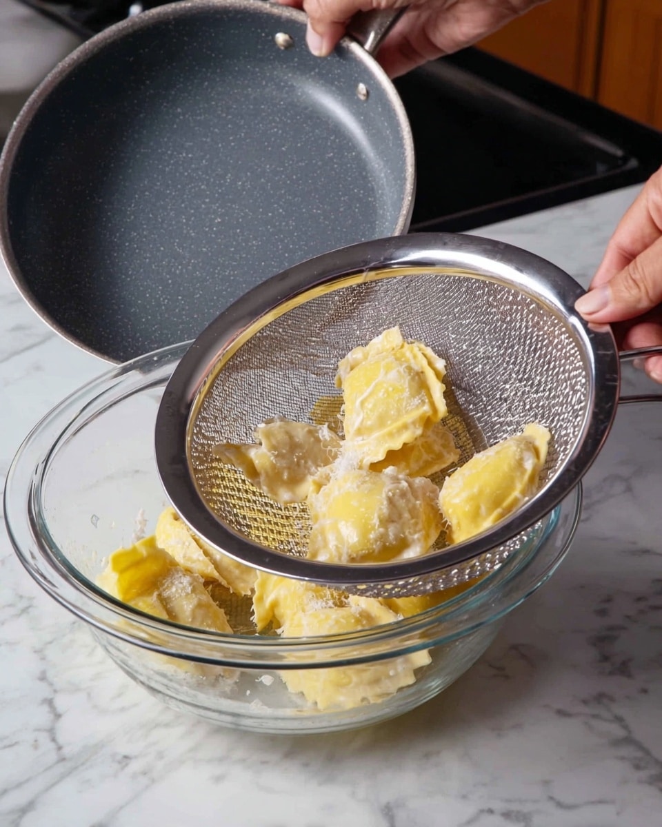 A close-up image showing a woman's hand holding a silver strainer over a clear glass bowl on a white marbled surface. Inside the strainer, there are several pieces of yellow stuffed ravioli with uneven shapes, covered in a light white creamy sauce. Another woman's hand is pouring the ravioli from a dark gray pan into the strainer. The setting is a kitchen countertop. Photo taken with an iphone --ar 4:5 --v 7