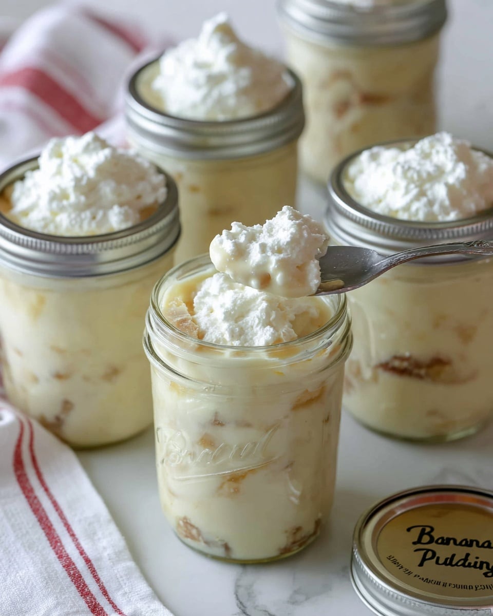 The image shows six clear glass jars filled with creamy banana pudding, arranged on a white marbled surface. Each jar has a silver metal lid, with one lid handwritten