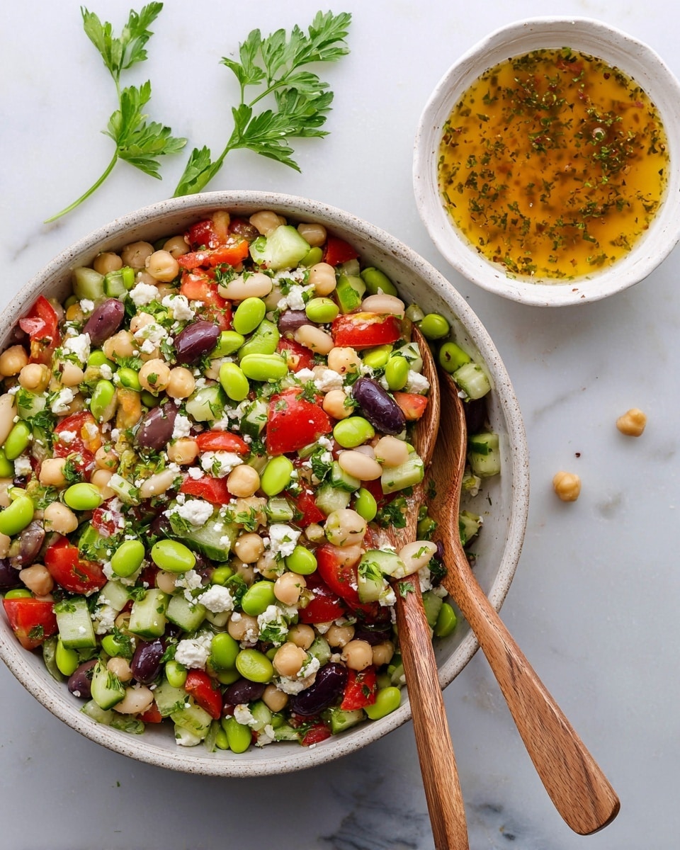 A large white bowl filled with different layers of fresh salad ingredients is placed on a white marbled surface. Starting from the bottom right, there are small chopped cucumber pieces in light green, followed by a layer of white beans in the bottom left. Above the beans, there is finely chopped white onion with green parsley sprinkled on top. On the left side, there are round beige chickpeas mixed with more green parsley. Across the top right side, there is a layer of bright green edamame beans. Crumbled white cheese is spread in the middle area with bright red cherry tomato halves scattered mainly on top of the cheese and partly over the other ingredients. The dish has a fresh and colorful look with carefully separated sections of each ingredient. A smaller white bowl sits above the salad bowl, and a brown bowl with some red sauce and a pink spatula is partially visible on the lower right corner. Photo taken with an iphone --ar 4:5 --v 7