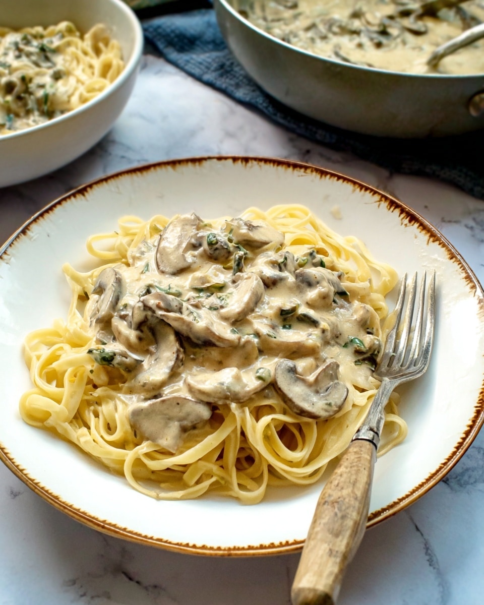 A white plate with a brown and gold rim holds a serving of light yellow pasta noodles arranged loosely in the bottom layer. On top, there is a creamy sauce with a pale beige color, speckled with soft mushroom slices and small green herb pieces mixed throughout. A fork with a worn light wooden handle rests on the edge of the plate, partially on the food. In the background, there are bowls with more creamy sauce and pasta visible, all placed on a white marbled surface. Photo taken with an iphone --ar 4:5 --v 7