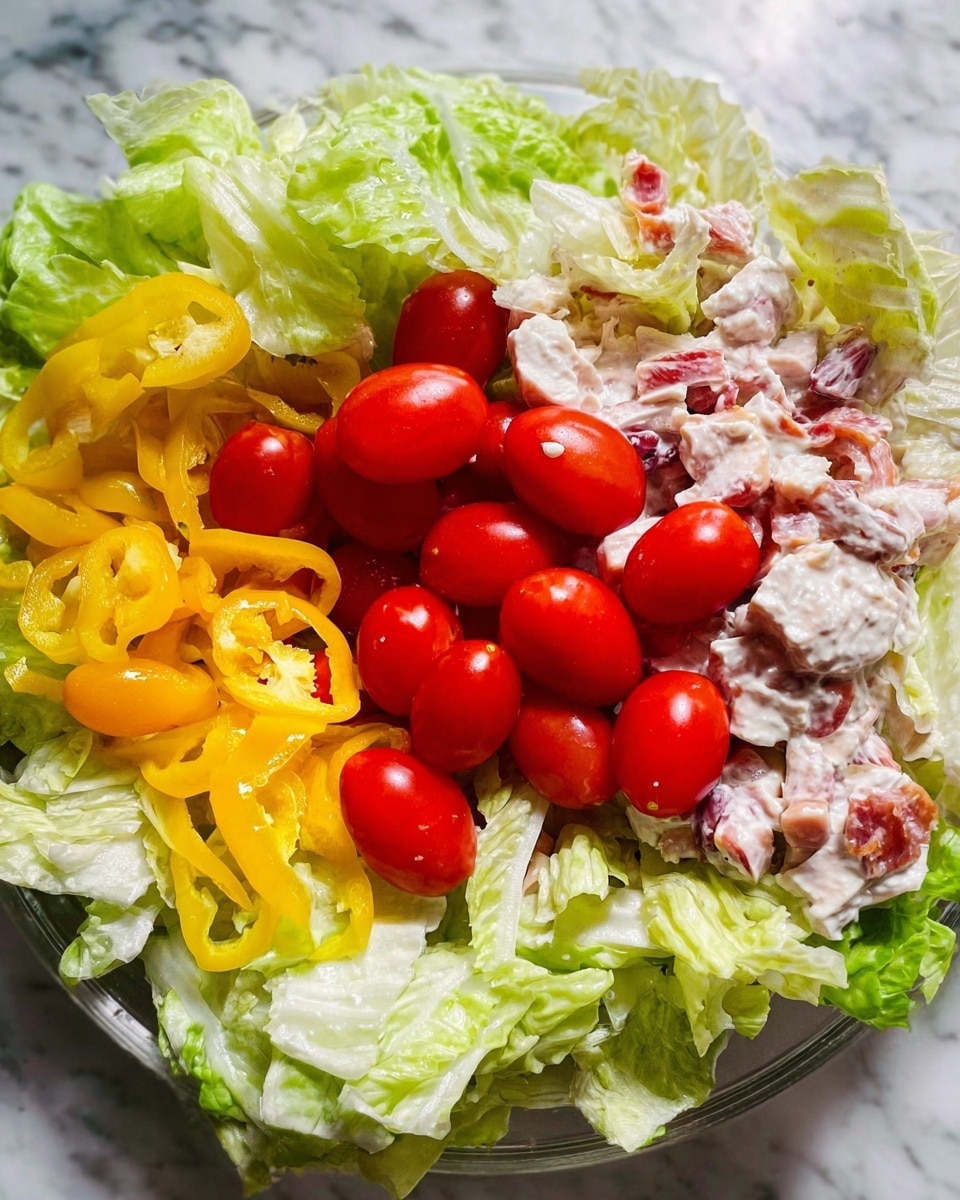 A dish shown with four main layers: the bottom layer is a mix of small chicken pieces with visible white creamy sauce and bits of pink ham, the second layer has a pile of bright yellow banana pepper rings scattered in one area, the third layer is a cluster of shiny red grape tomatoes placed in the center, and the top layer is fresh light green lettuce leaves torn into medium pieces spread around the tomatoes on the white marbled surface photo taken with an iphone --ar 4:5 --v 7