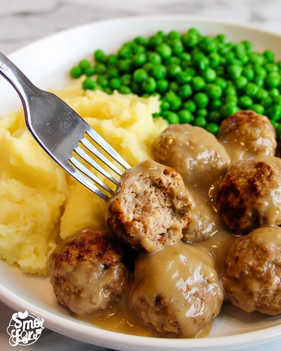 The image shows a white plate filled with several brown meatballs covered in a light brown sauce. Behind the meatballs, there is a layer of pale yellow mashed potatoes with a smooth texture. On the upper side of the plate, there is a pile of bright green peas, adding a fresh color contrast. A silver fork is pressing into one meatball, breaking it open to show the inside. The plate is placed on a white marbled surface. Photo taken with an iphone --ar 4:5 --v 7