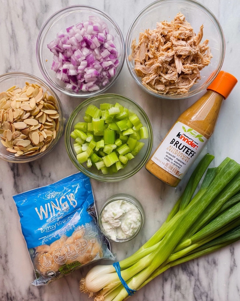 The image shows a white marbled surface with several cooking ingredients arranged neatly. There are three glass containers: one with chopped red onions in the top left, one with shredded light brown chicken in the top right, and one with diced green celery at the bottom center. Below the celery container is a tall bottle of Kinder's Wing Sauce & Dip labeled