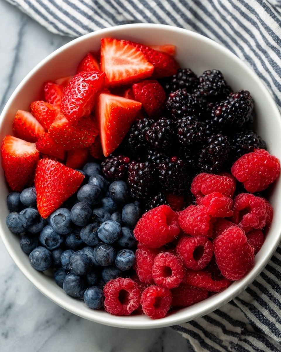 A white bowl filled with four sections of fresh berries arranged in layers: the top left section has bright red strawberries cut into halves showing their juicy inner texture, the top right section has dark, shiny blackberries, the bottom right section has vibrant red raspberries with their hollow centers visible, and the bottom left section is full of round, blue blueberries. The bowl sits on a white marbled surface with a striped cloth in the background. photo taken with an iphone --ar 4:5 --v 7