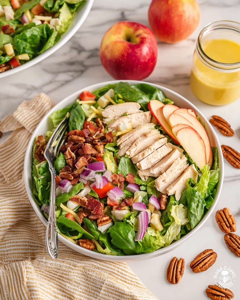 A white bowl filled with a fresh salad showing three distinctive layers: the bottom layer is a mix of green leafy lettuce and spinach, the middle layer has small diced red tomatoes, thin slices of purple onion, and chunks of light yellow cheese, while the top layer features several slices of light tan cooked chicken pieces and whole pecans scattered throughout. A silver fork rests inside the bowl on the left side. Next to the bowl, on a white marbled surface with a beige striped cloth underneath, are slices of red and yellow apple along with whole pecans scattered, and a clear glass jar with yellow dressing. A large bowl of extra salad sits at the top left of the image. photo taken with an iphone --ar 4:5 --v 7