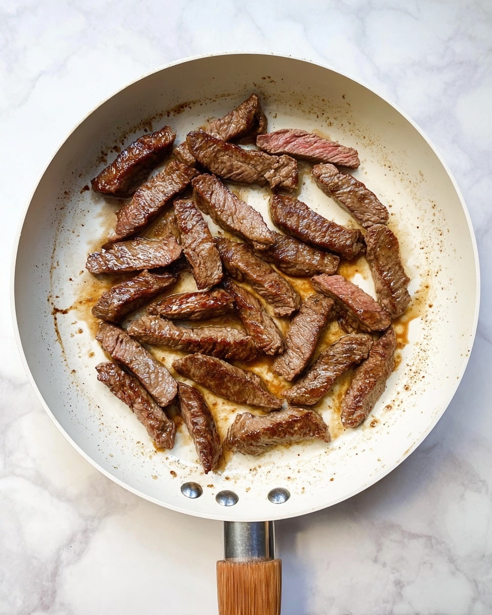 A white frying pan with a wooden handle sits on a white marbled surface. Inside the pan, there are about twenty small strips of cooked beef arranged mostly in a circular pattern with some in the center. The beef strips have a browned and slightly crispy outer texture with visible grill marks and a juicy interior showing a pinkish center. The bottom of the pan has a thin layer of brown cooking juices spreading unevenly around the beef. The pan’s edge and base show slight browning from cooking. photo taken with an iphone --ar 4:5 --v 7