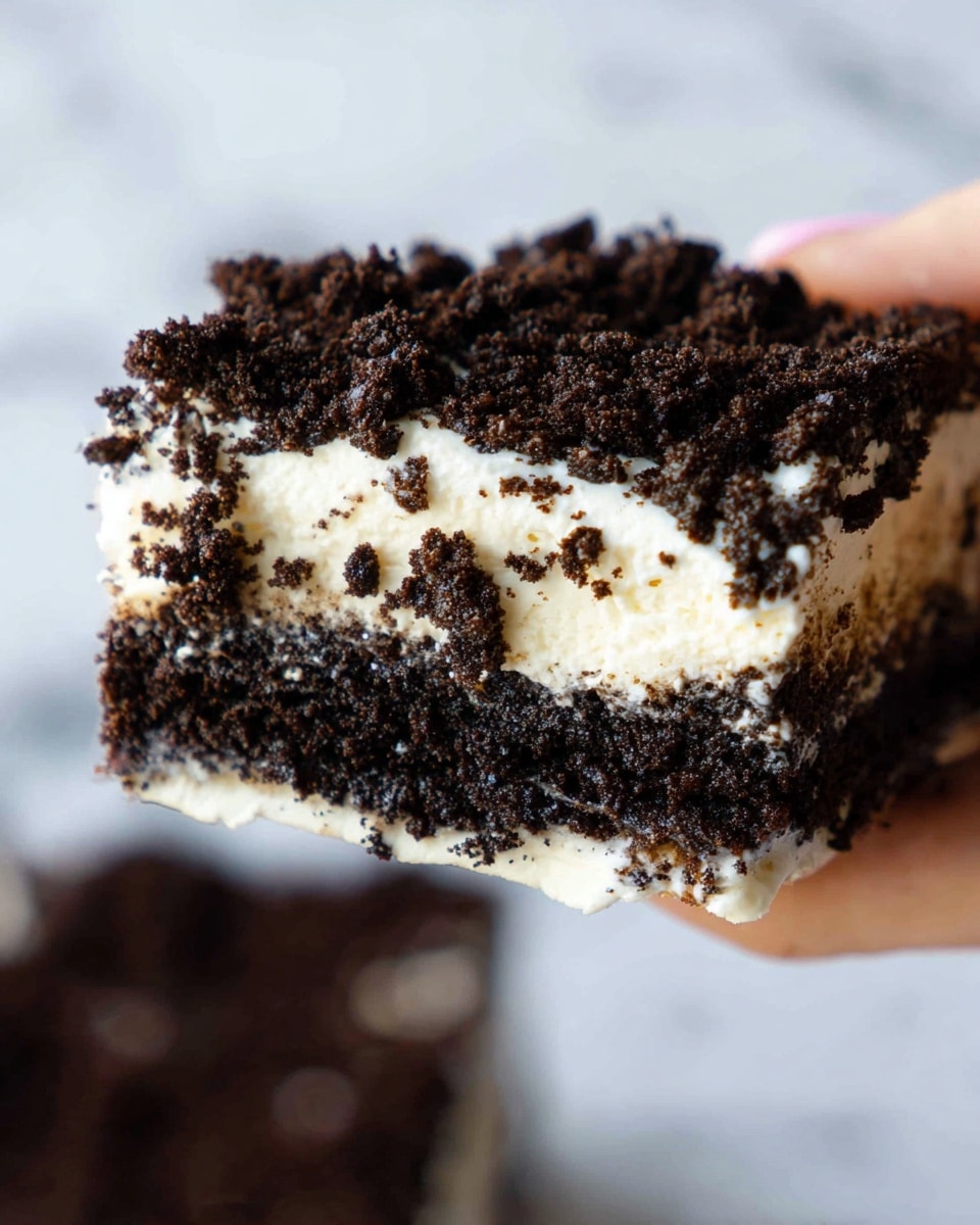 A close-up view of a layered dessert held by a woman's hand, showing three main layers: a bottom dark brown crumb layer that looks like crushed cookies, a middle thick creamy white layer, and a top layer heavily covered with more dark brown crumbled cookie pieces. The dessert has a textured and rough surface from the crumbles, contrasting with the smooth cream layer beneath. The background features a white marbled texture, giving a clean and bright look. photo taken with an iphone --ar 4:5 --v 7