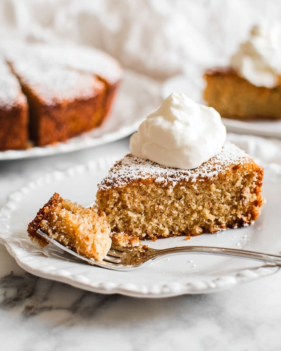 A slice of light brown cake with a slightly crumbly texture is placed on a white plate with a scalloped edge. The cake has a dusting of white powdered sugar on top and a dollop of white whipped cream resting on the upper right side. In front of the slice, a silver fork holds a piece of the cake, showing its moist and soft inside. The background has a blurred white marbled texture, with another similar cake slice visible on a white plate. Photo taken with an iphone --ar 4:5 --v 7