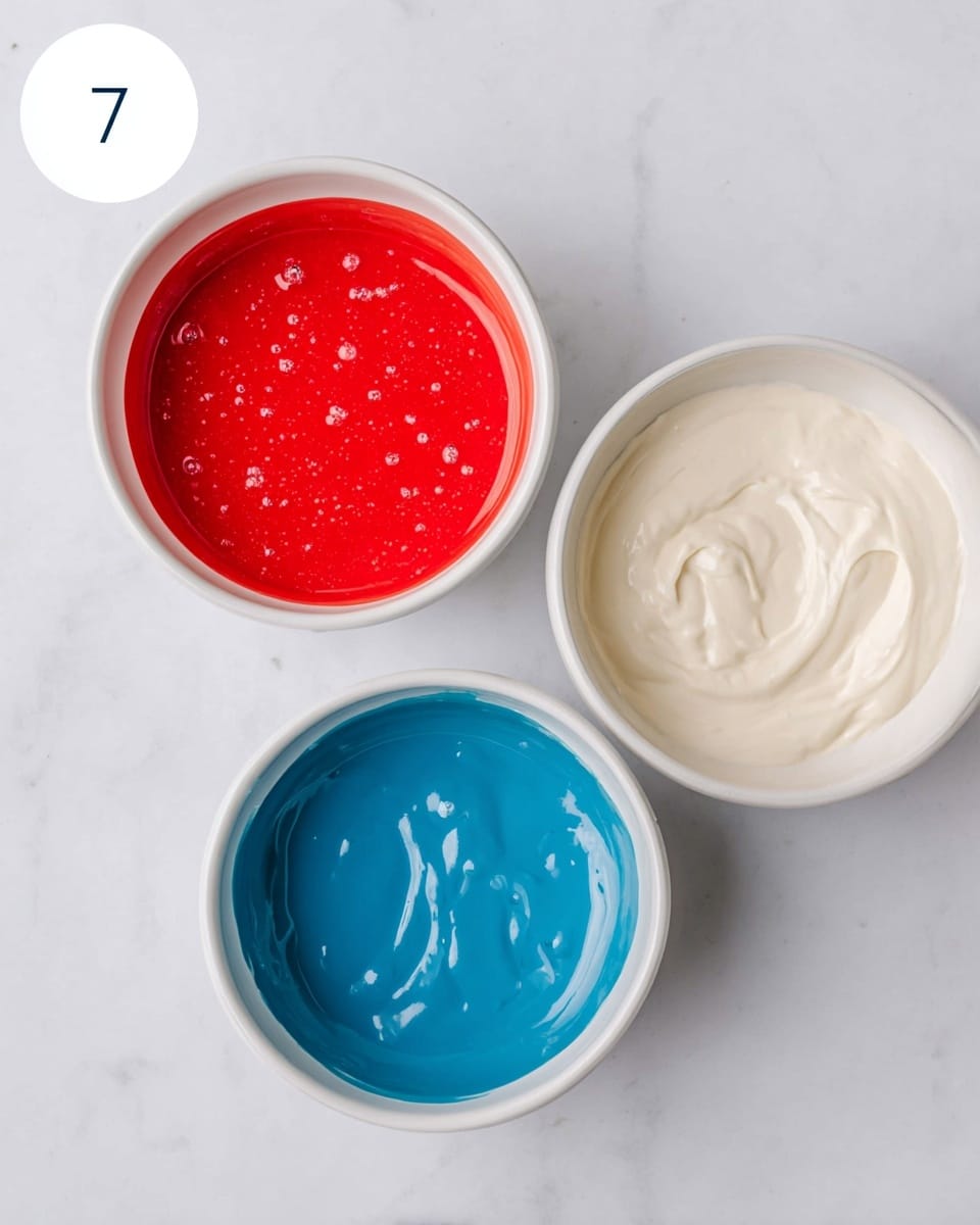 Three round white bowls are placed on a white marbled surface, arranged in a loose triangle. The top left bowl is filled with a smooth, bright red liquid that has tiny bubbles scattered on its surface. The top right bowl holds a thick, creamy off-white mixture with a few light swirls. The bottom bowl contains a smooth, vibrant blue liquid with some small light reflections. A white circle with a bold black number 7 is positioned near the top left bowl. photo taken with an iphone --ar 4:5 --v 7