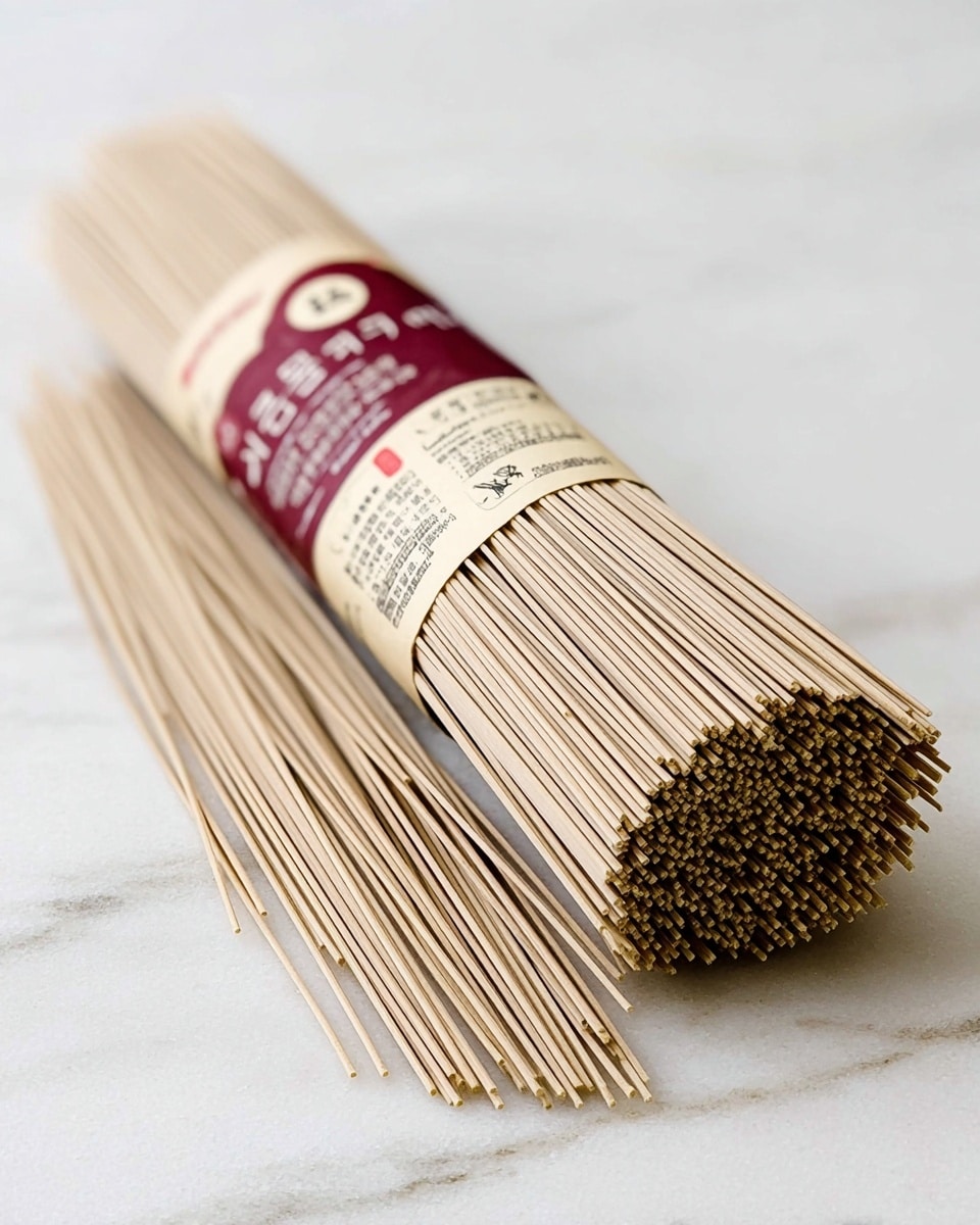 A bundle of light brown thin noodles tied together with a cream and maroon paper label wrapped around its middle, showing text in black and red with some smaller text in light gray. The noodles are long and straight, with some loose noodles spread beside the bundle on a white marbled surface. The texture of the noodles is smooth and firm, with tightly packed ends facing the camera. Photo taken with an iphone --ar 4:5 --v 7