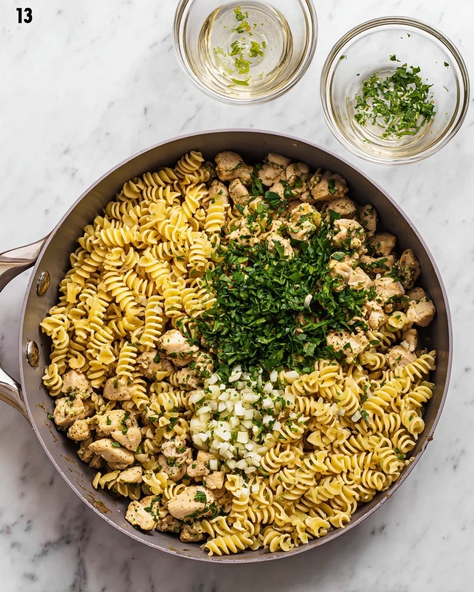 A large gray cooking pan filled with three layers of food: the bottom layer is a mix of small cooked chicken pieces and chopped green herbs, the middle layer features pale yellow spiral pasta with a ridged texture, and the top layer shows a scattering of fresh green parsley leaves and small white garlic slices mixed evenly throughout. The pan rests on a white marbled surface. Above the pan are two small empty clear glass bowls with a few green herb bits stuck inside one of them. Photo taken with an iphone --ar 4:5 --v 7