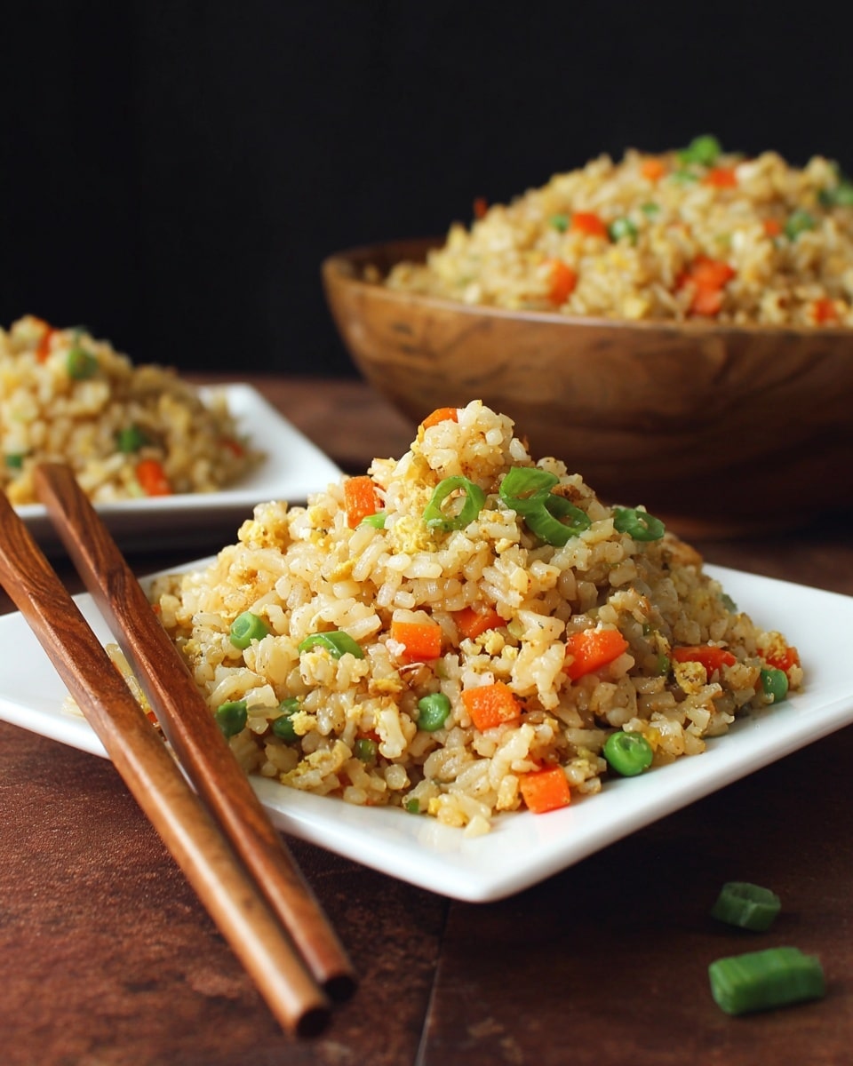A close-up of a serving of fried rice on a white square plate with two wooden chopsticks resting on the plate's left side. The fried rice is light brown with small diced orange carrots and bright green chopped scallions mixed evenly throughout. In the blurry background, there is a large rustic wooden bowl filled with more fried rice, featuring the same colors and ingredients. The scene is set on a deep brown table with a white marbled texture surface visible near the plate, and the background is black, creating strong contrast with the dish. Photo taken with an iphone --ar 4:5 --v 7