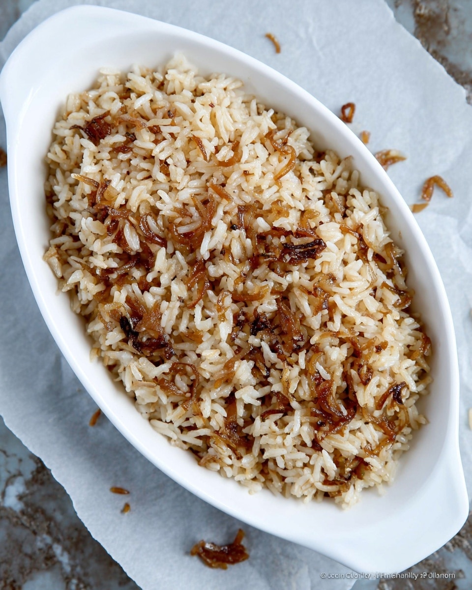 A white oval-shaped dish holds a single layer of cooked rice mixed with pieces of caramelized onions, giving it a varied light and dark brown color. The rice grains are separated and have a slightly shiny texture, with some scattered around the dish on a sheet of parchment paper. The background surface is a white marbled texture. Photo taken with an iphone --ar 4:5 --v 7