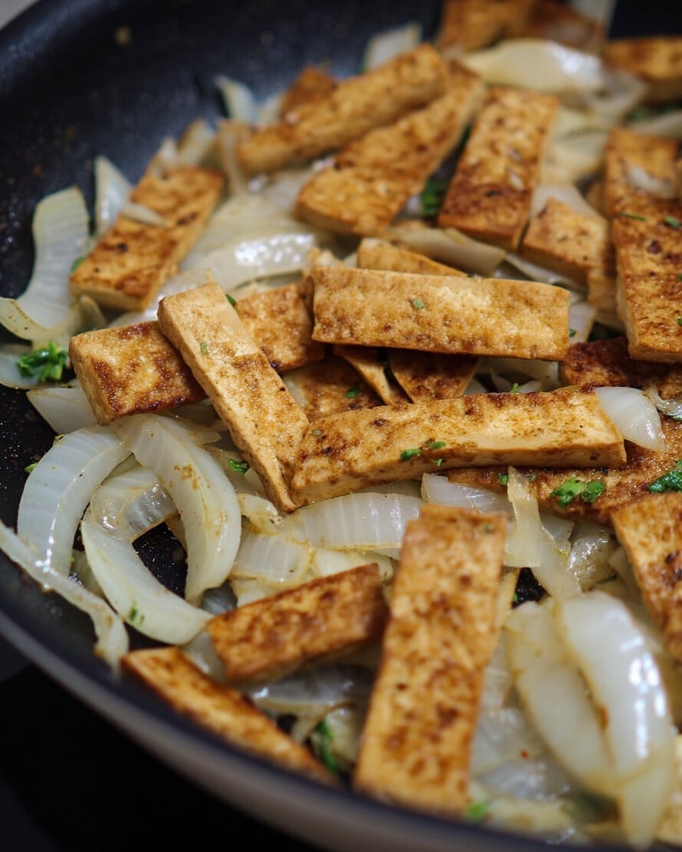 The image shows a dish in a black pan with two main layers: the bottom layer has sautéed white onion slices that look soft and slightly shiny, and the top layer is made of browned rectangular tofu pieces with a light golden color and a slightly crispy texture. Small bits of green herbs are scattered among the tofu and onions, adding a touch of color. The white marbled texture is visible just around the edges of the pan. Photo taken with an iphone --ar 4:5 --v 7