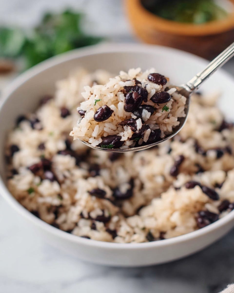 A close-up of a spoon holding a mix of white rice and small black beans above a white bowl filled with the same rice and black beans mixture. The grains of rice are soft and separate, mixed evenly with the black beans, creating a speckled pattern of light beige and dark purple-black colors. The background shows some blurry green leaves and a small wooden bowl with green food, all set on a white marbled surface. The photo taken with an iphone --ar 4:5 --v 7