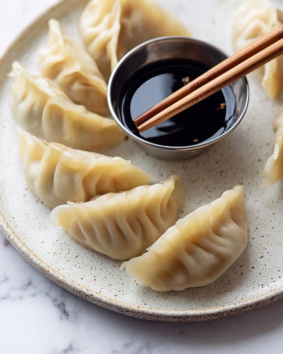 The image shows a close-up of several light beige dumplings arranged in a curved line on a white plate with a speckled texture. The dumplings have delicate folds along the top edges, creating a soft, pleated look. In the center background, there is a small metal cup filled with dark soy sauce, featuring a shiny surface that reflects light. On top of the cup sit a pair of thin wooden chopsticks positioned horizontally. The plate rests on a white marbled surface. photo taken with an iphone --ar 4:5 --v 7