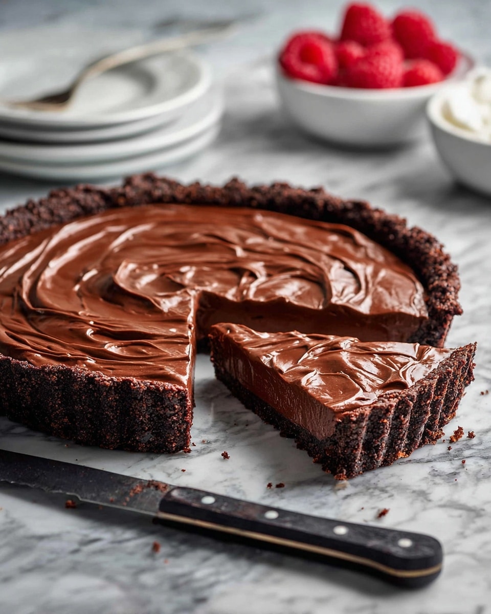 A two-layer chocolate tart is shown with a dark, crumbly crust forming the base and sides, looking rough and textured. The top layer is smooth, rich chocolate filling with swirled patterns giving it a glossy, creamy look. The tart has one slice partly pulled out, showing the thickness of the filling and crust. It sits on a surface with a white marbled texture, and near the tart is a knife with a dark handle and silver dots. In the blurry background, there are white bowls stacked and another white bowl filled with bright red raspberries scattered around. photo taken with an iphone --ar 4:5 --v 7
