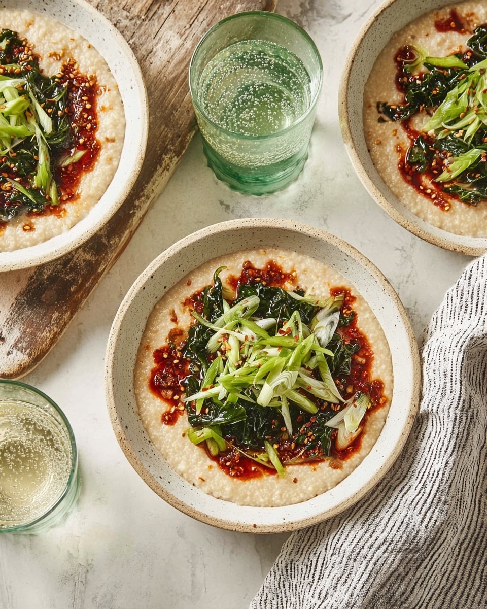 Three white speckled bowls are shown on a white marbled surface. Each bowl has a creamy beige porridge base so smooth it fills almost to the edge. The porridge is topped with several patches of deep red chili oil spread unevenly on the surface. Over the chili oil, there is a layer of wilted dark green leafy vegetables in the center. Thinly sliced light green scallions scatter over the top, adding freshness and light color contrast. Next to the bowls, there is a glass filled with bubbly clear liquid in a green glass on the same surface. A folded light gray tea towel with black and white stripes rests near the bottom right corner, and a rustic wooden board sits under one bowl at the top. photo taken with an iphone --ar 4:5 --v 7