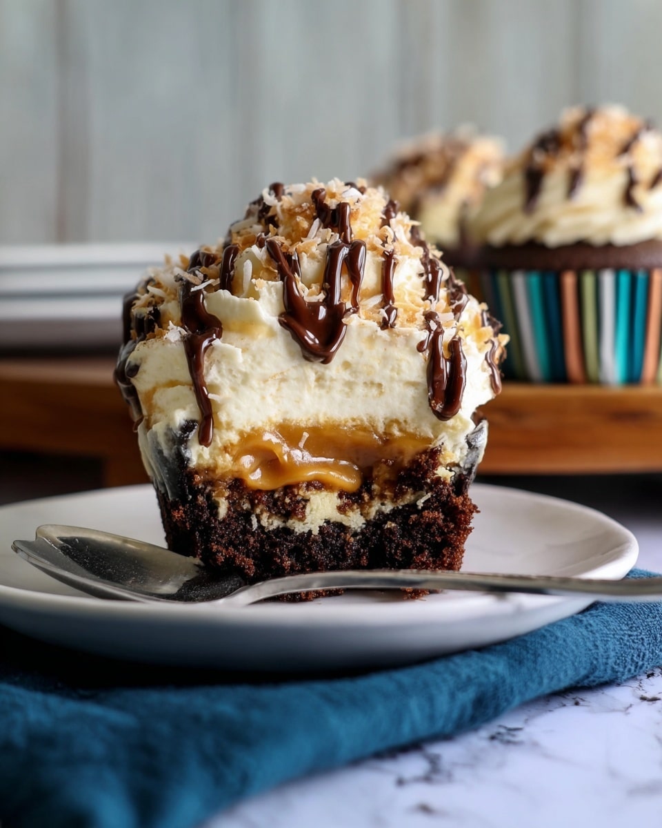 A cupcake is shown on a white plate with a silver spoon resting on a dark blue cloth beside it. The cupcake has three main layers: the bottom layer is dark brown chocolate cake, the middle layer is a moist caramel filling, and the top layer is creamy light beige frosting. Toasted coconut flakes and dark chocolate drizzle decorate the top. Another cupcake in a striped paper liner sits blurred in the background on a wooden surface, all set on a white marbled texture surface. photo taken with an iphone --ar 4:5 --v 7