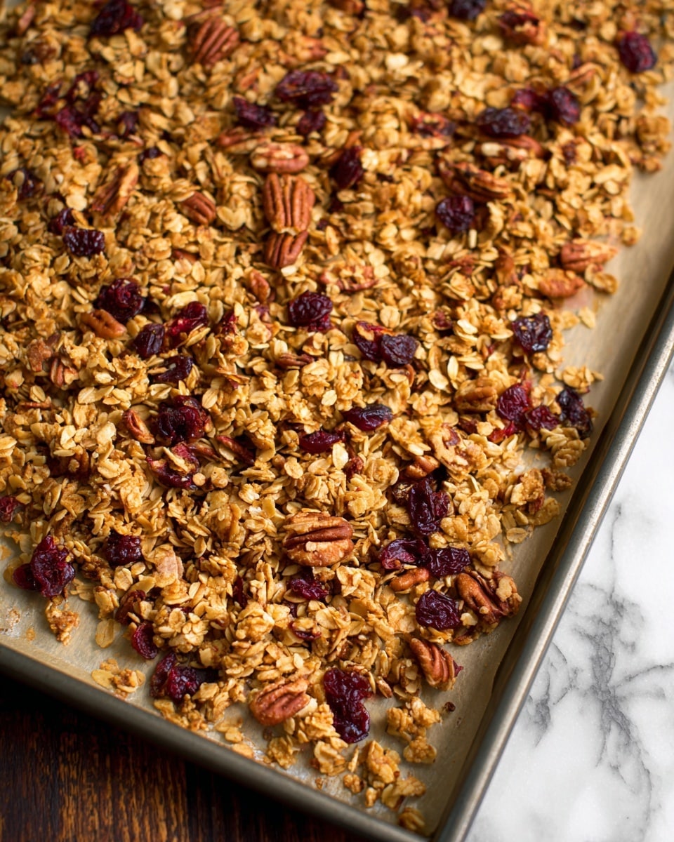 A close-up view of a baking tray filled with granola spread out evenly on parchment paper. The granola has a rough texture made from golden oatmeal flakes mixed with deep brown pecans and scattered dark red dried cranberries. The layers are flat with clusters of oats and nuts loosely touching each other across the light beige parchment, showing a natural and textured look. The tray rests on a dark wooden surface, but the background is changed to white marbled texture. Photo taken with an iphone --ar 4:5 --v 7