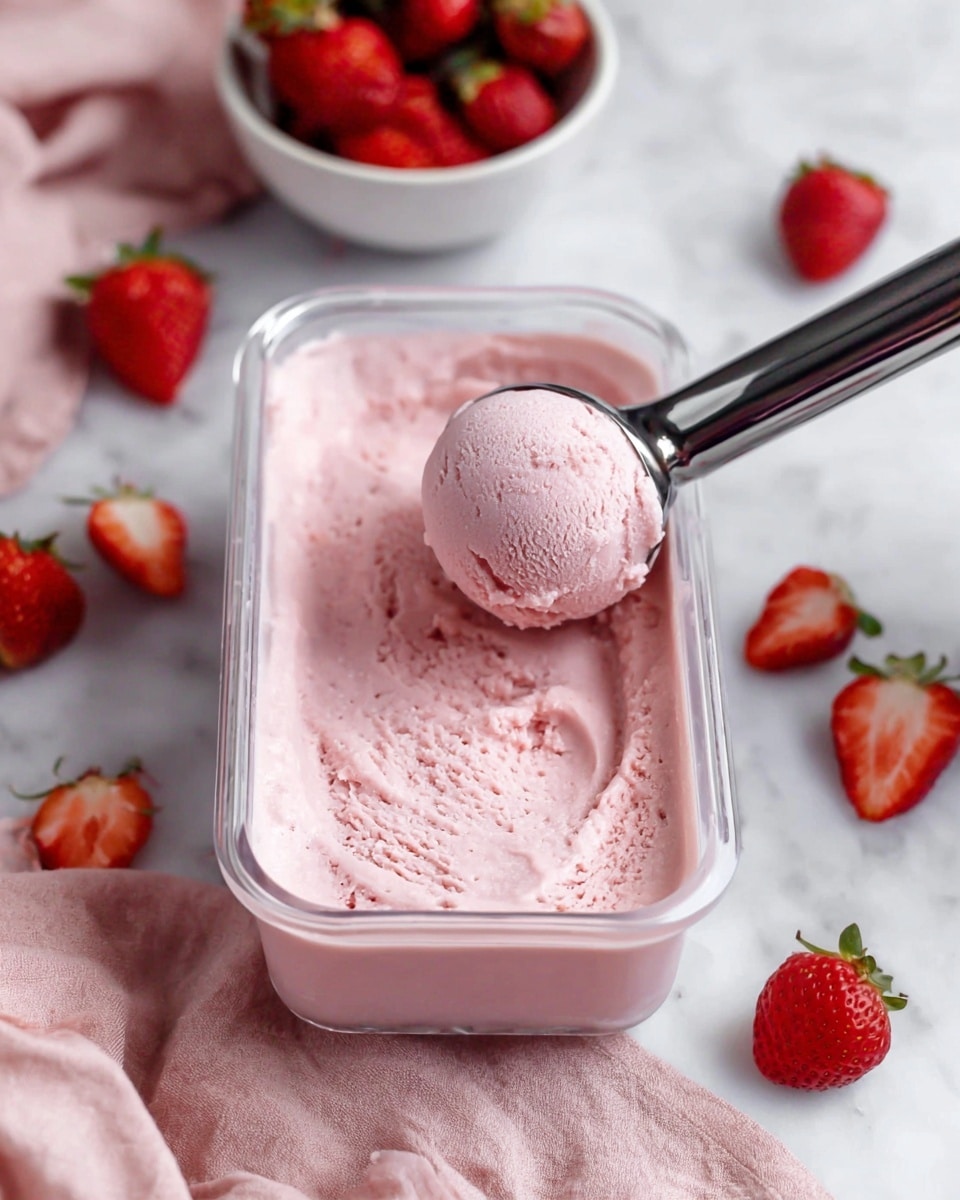 A clear rectangular container filled with smooth, light pink ice cream is placed on a white marbled surface. A silver ice cream scoop is lifting a round, creamy pink scoop from the container. Around the container, fresh whole and halved strawberries lie scattered, along with a white bowl full of ripe red strawberries in the background. A soft pink cloth rests partially under the container, adding a gentle color contrast. Photo taken with an iphone --ar 4:5 --v 7