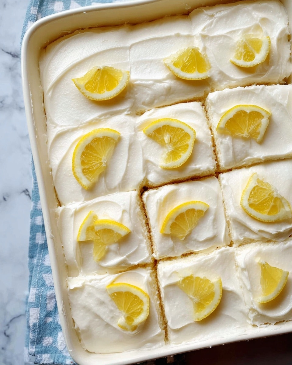 The dish shows a white pan filled with a square, soft cake that is covered in a smooth white frosting. The cake is divided into neat square pieces, each topped with a bright yellow lemon slice placed in the center. The frosting has a creamy texture with slight swirls and a thick layer covering the entire surface, with the edges slightly uneven. The background features a white marbled surface under the pan. photo taken with an iphone --ar 4:5 --v 7