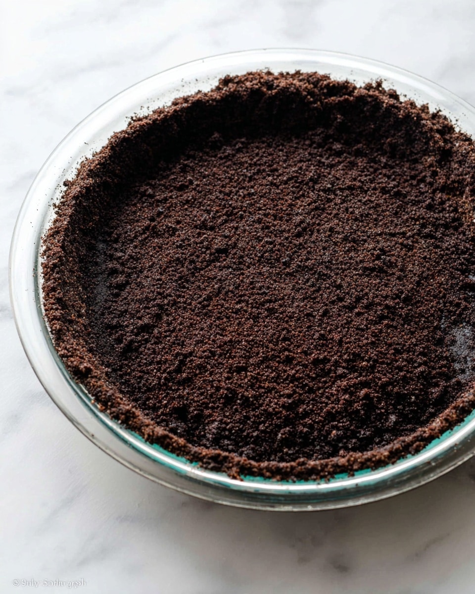 A close-up view of a creamy cookies and cream pie with three visible layers: a dark crumbly cookie crust forming the bottom and sides, a thick light cream filling mixed with small cookie crumbs in the middle, and five swirls of smooth white whipped cream arranged evenly on top near the crust edge. A slice is partially removed showing the inside texture, with a whole cookie placed on the side near the cut. The pie is in a clear glass dish set on a white marbled surface, with a green cloth blurred in the background. photo taken with an iphone --ar 4:5 --v 7