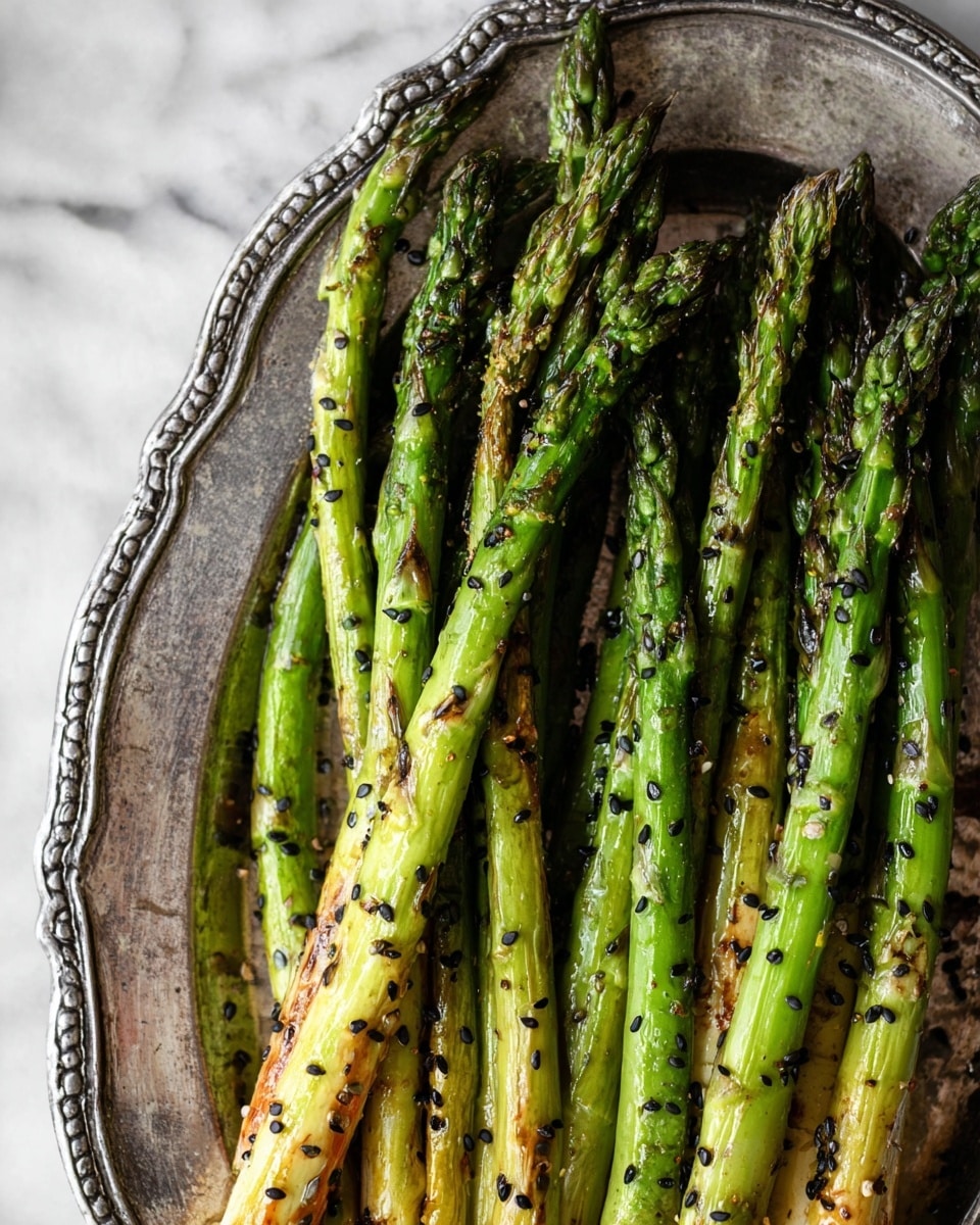 In a vintage silver tray with intricate edges, there are around twelve long roasted asparagus stalks arranged close together. The asparagus stalks are mainly bright green with lightly browned, slightly charred spots showing a mix of smooth and wrinkled textures. Scattered small black sesame seeds and coarse spices are visible on the stalks, adding a textured contrast to their shiny, roasted surfaces. The tray rests on a white marbled surface and the lighting highlights the asparagus tips and seasoning details clearly. Photo taken with an iphone --ar 4:5 --v 7